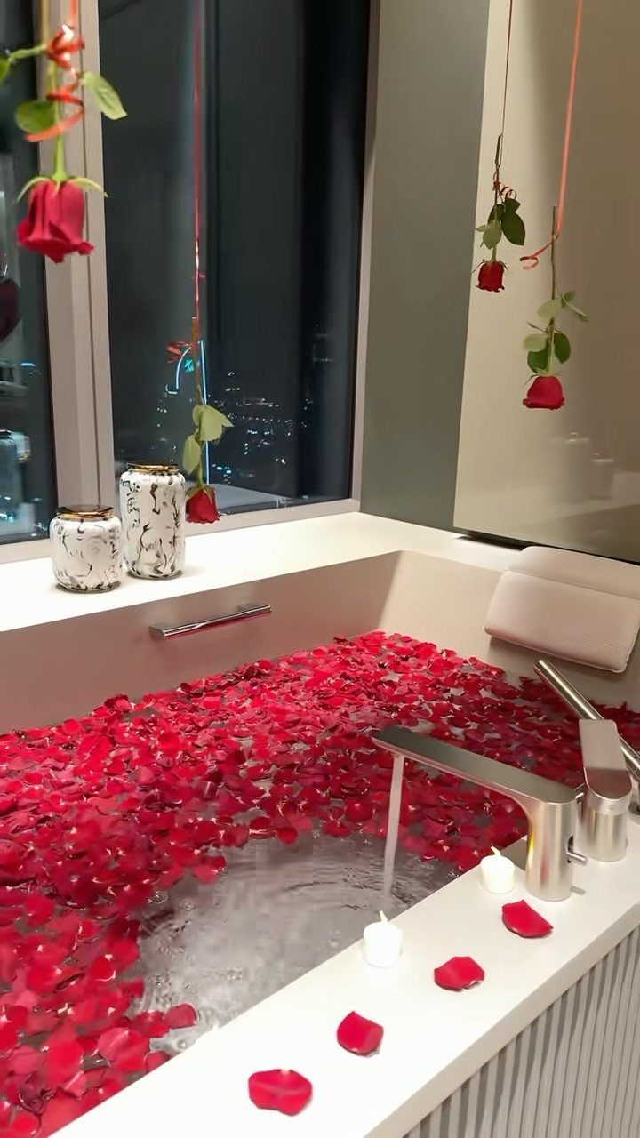 Bathtub filled with red rose petals and candles for a romantic anniversary celebration.