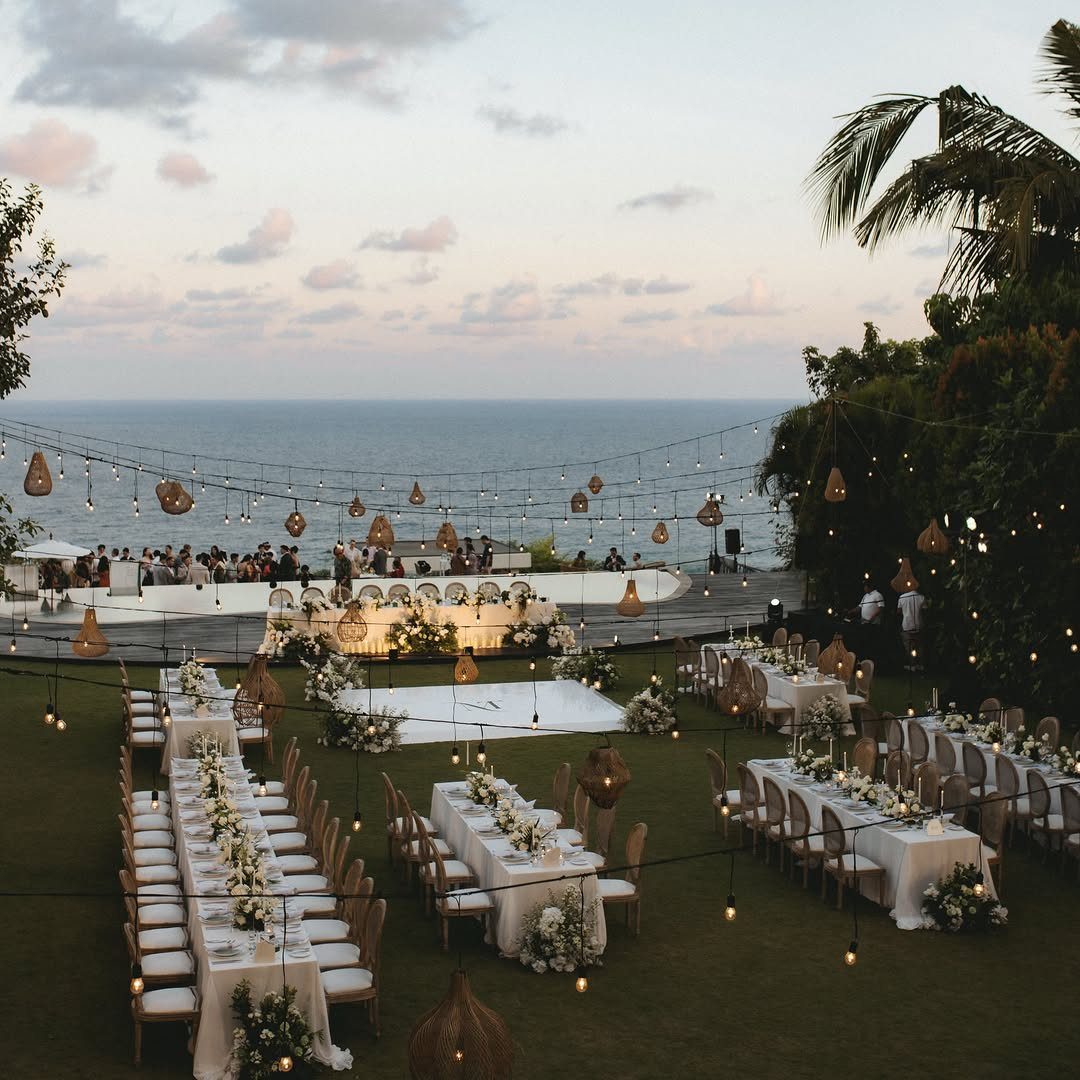 Outdoor wedding reception on a lawn with white tables overlooking the ocean at dusk