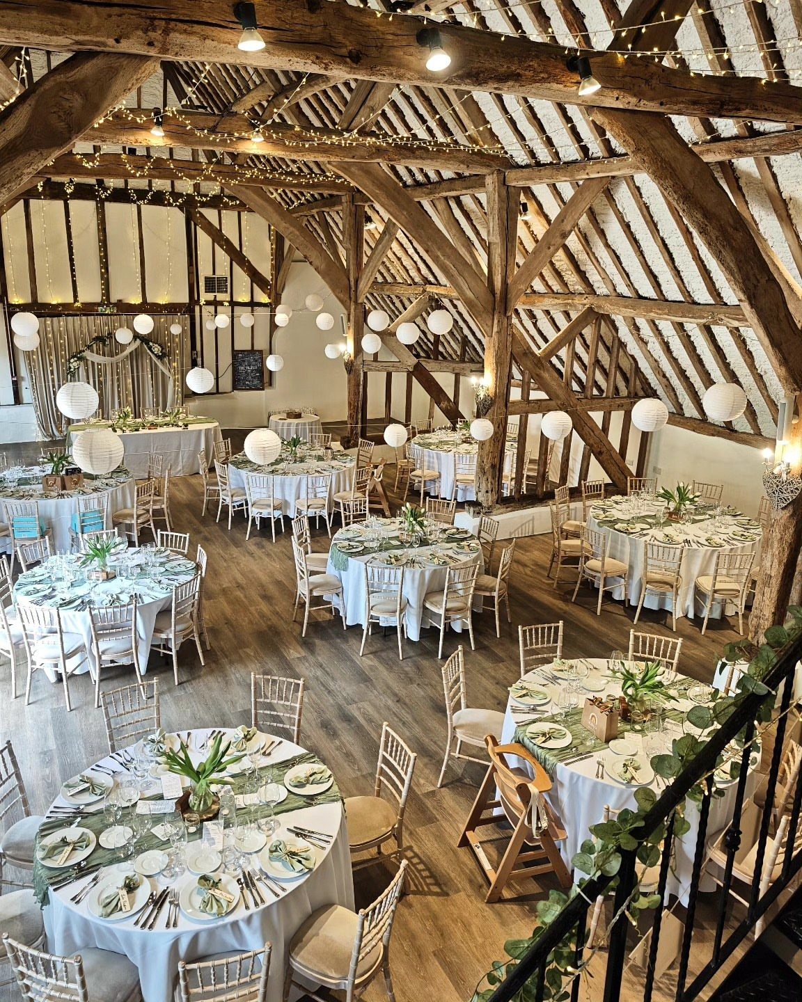 Rustic barn interior with round wedding tables under exposed wooden beams and string lights.