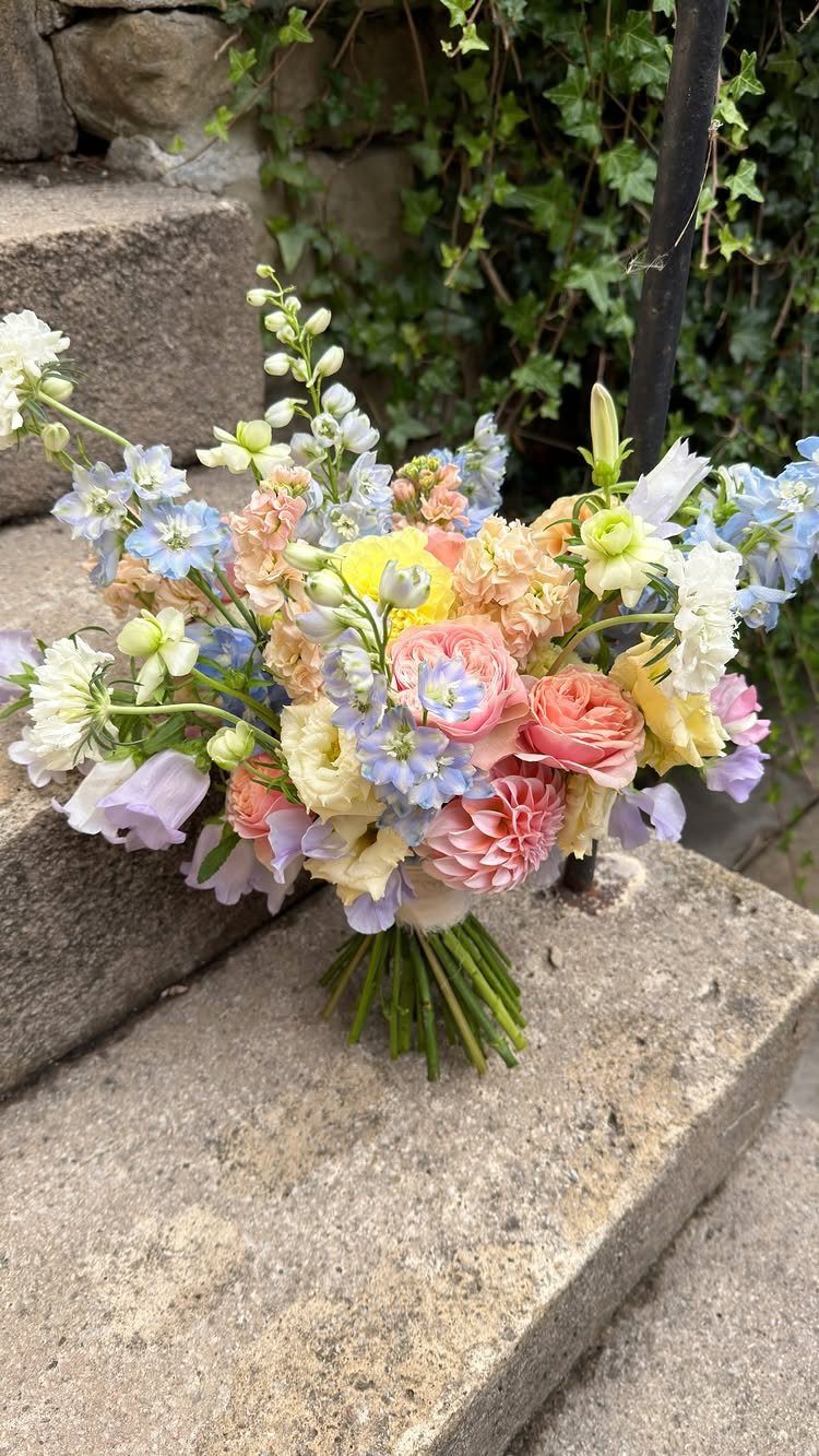 Pastel bridal bouquet with pink and blue flowers resting on stone steps.