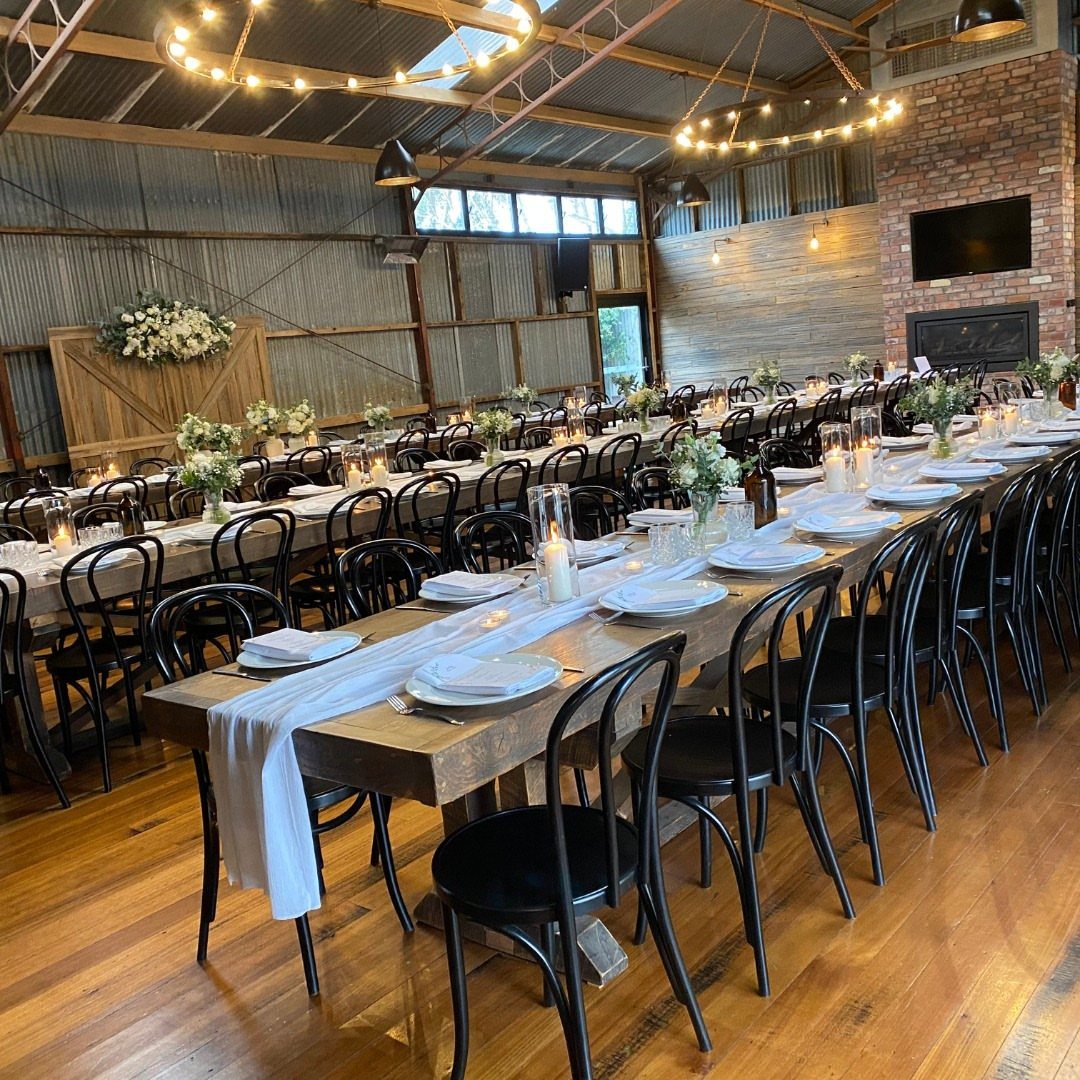 Long wooden wedding tables with white runners and floral centerpieces in a rustic barn.