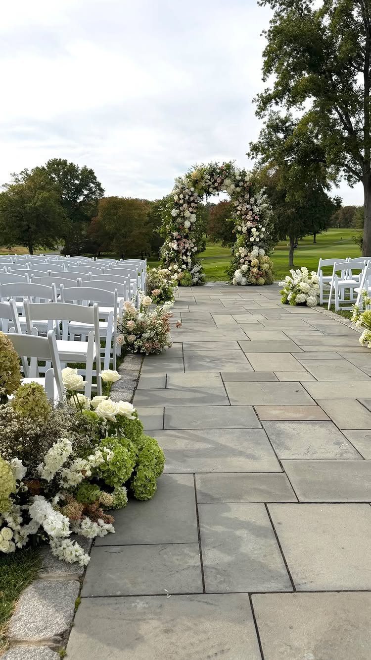 Floral wedding arch and white chairs along a stone path in a field