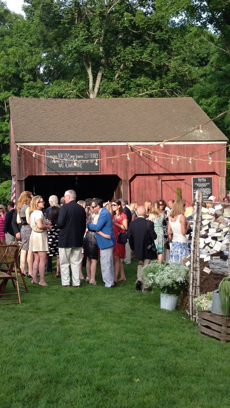 Guests gathering on a green lawn in front of a red wedding barn.