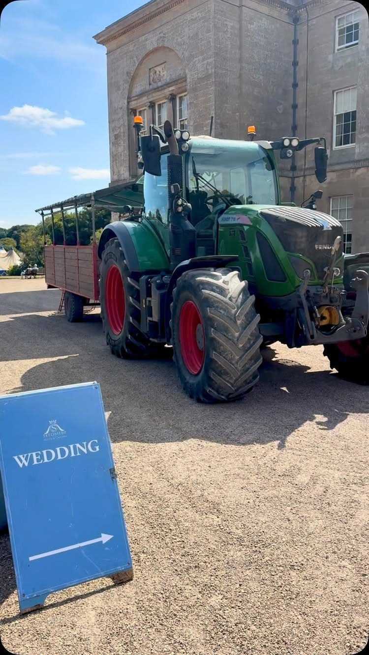 Green tractor with passenger trailer and wedding directional sign on gravel driveway