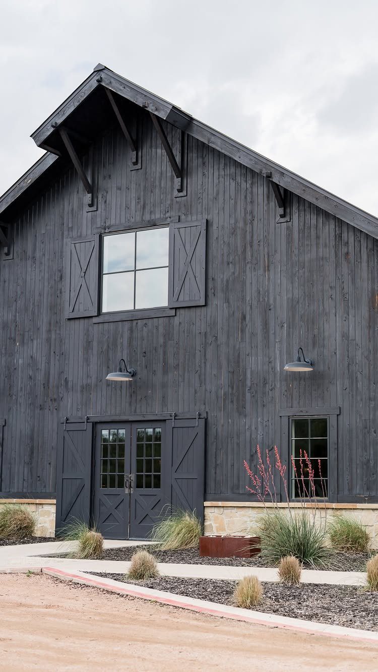 Black wooden barn with gabled roof and stone foundation under a cloudy sky