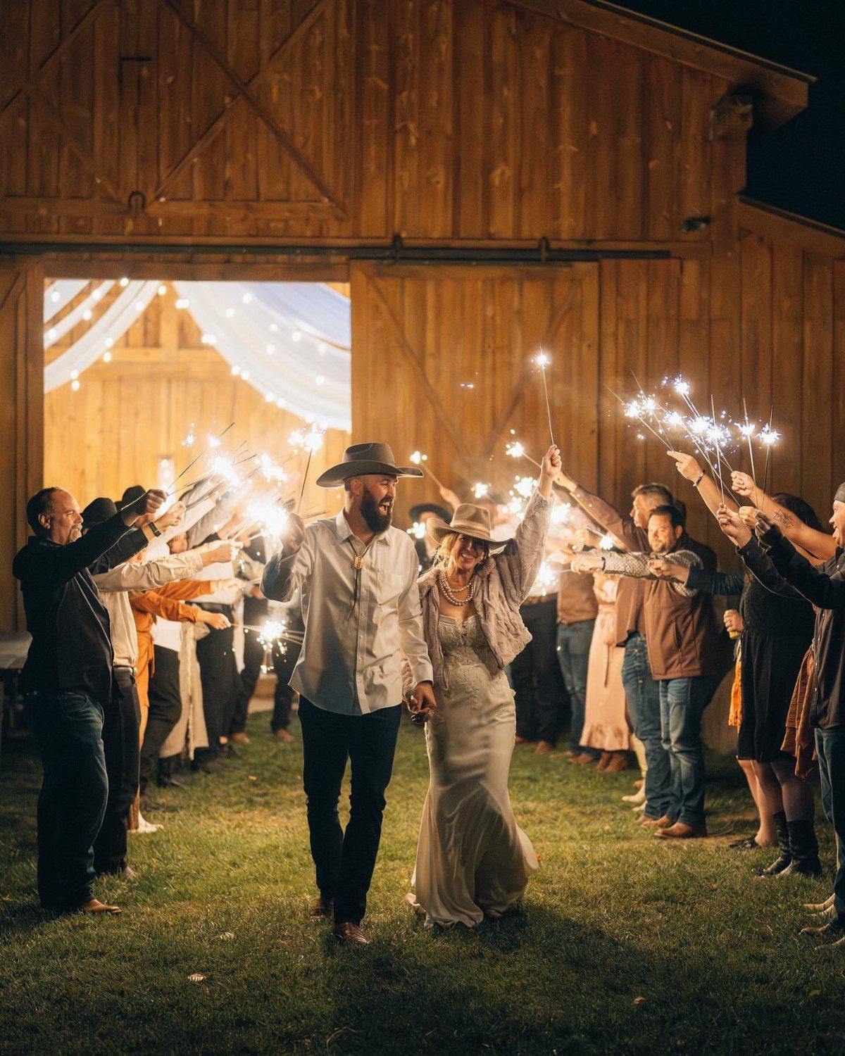 Bride and groom walking through a sparkler send-off in front of a wooden barn