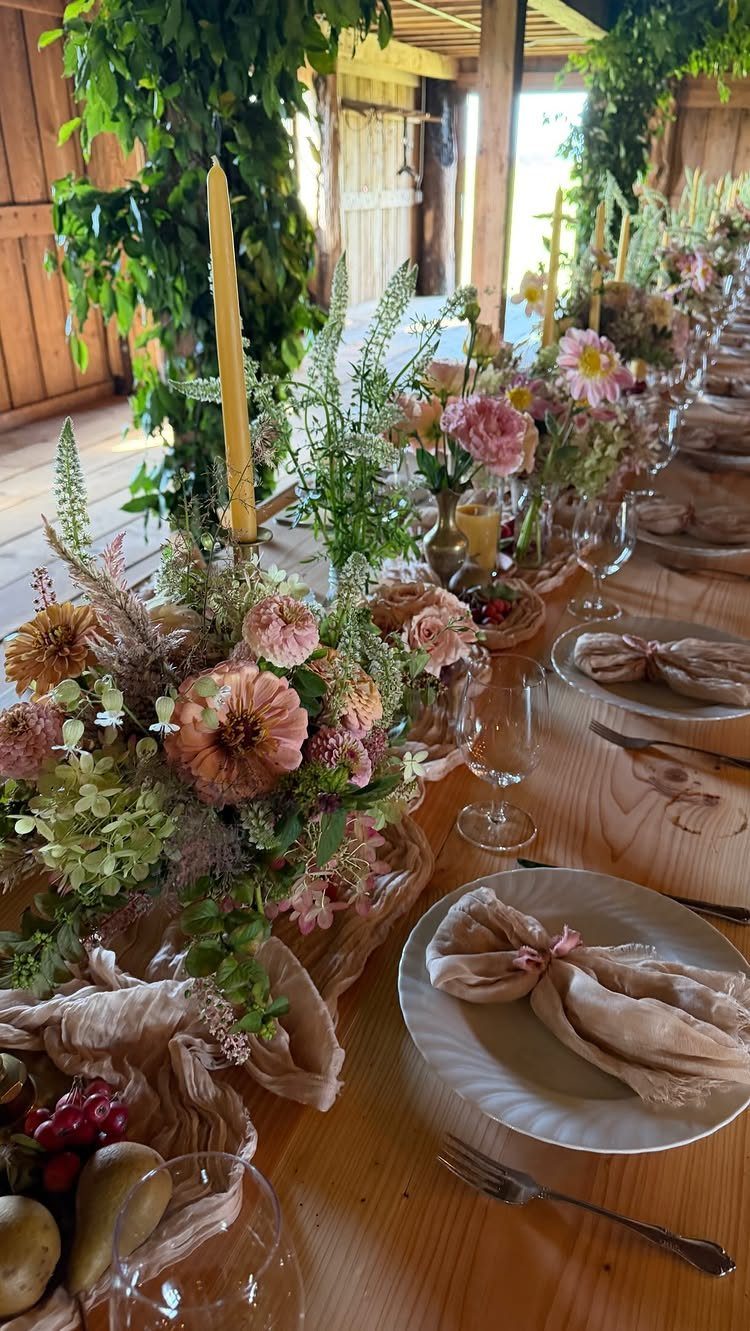 Floral centerpieces and yellow candles on a wooden table in a rustic barn.