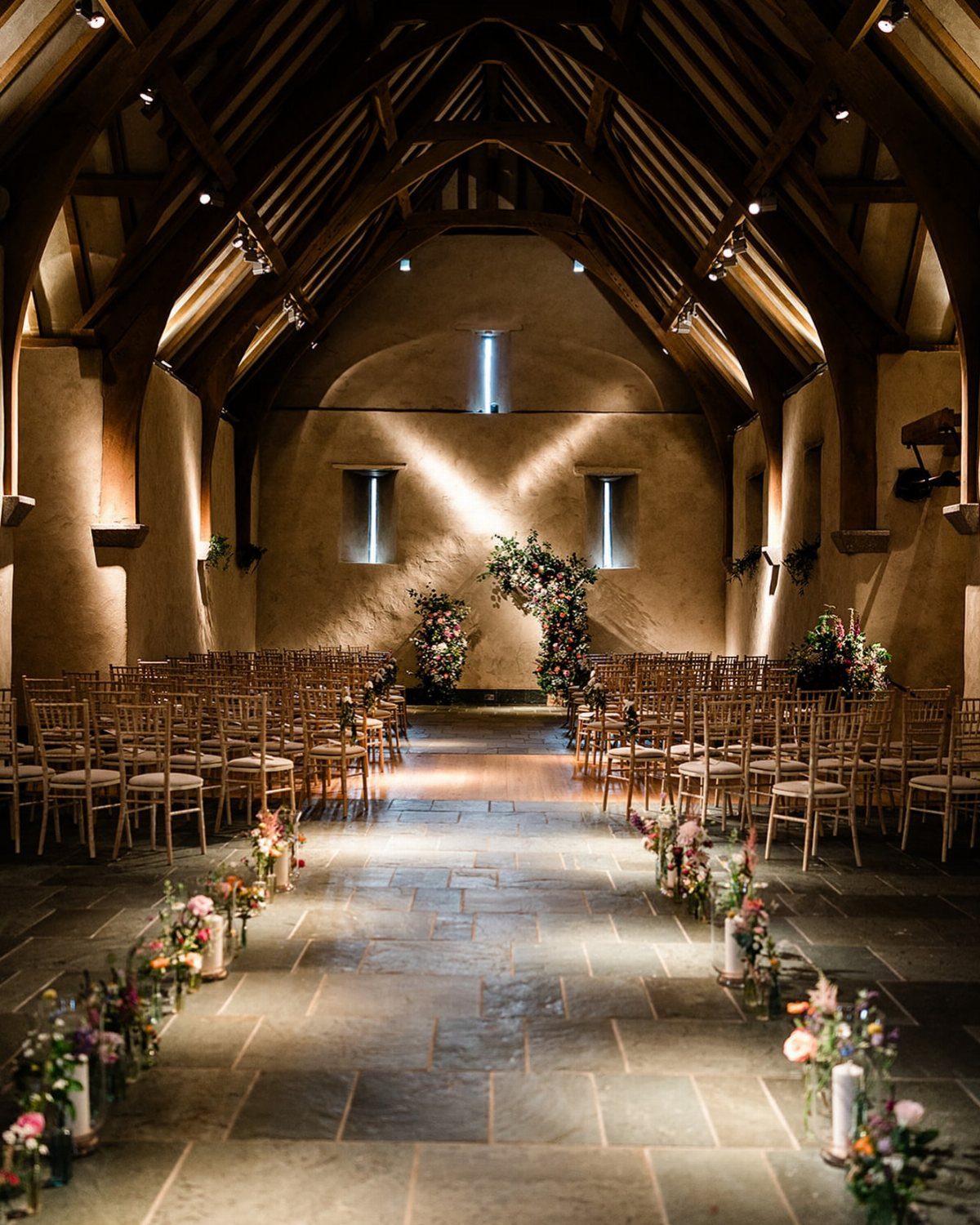 Wedding ceremony setup in a rustic barn with timber ceilings and floral aisle decor