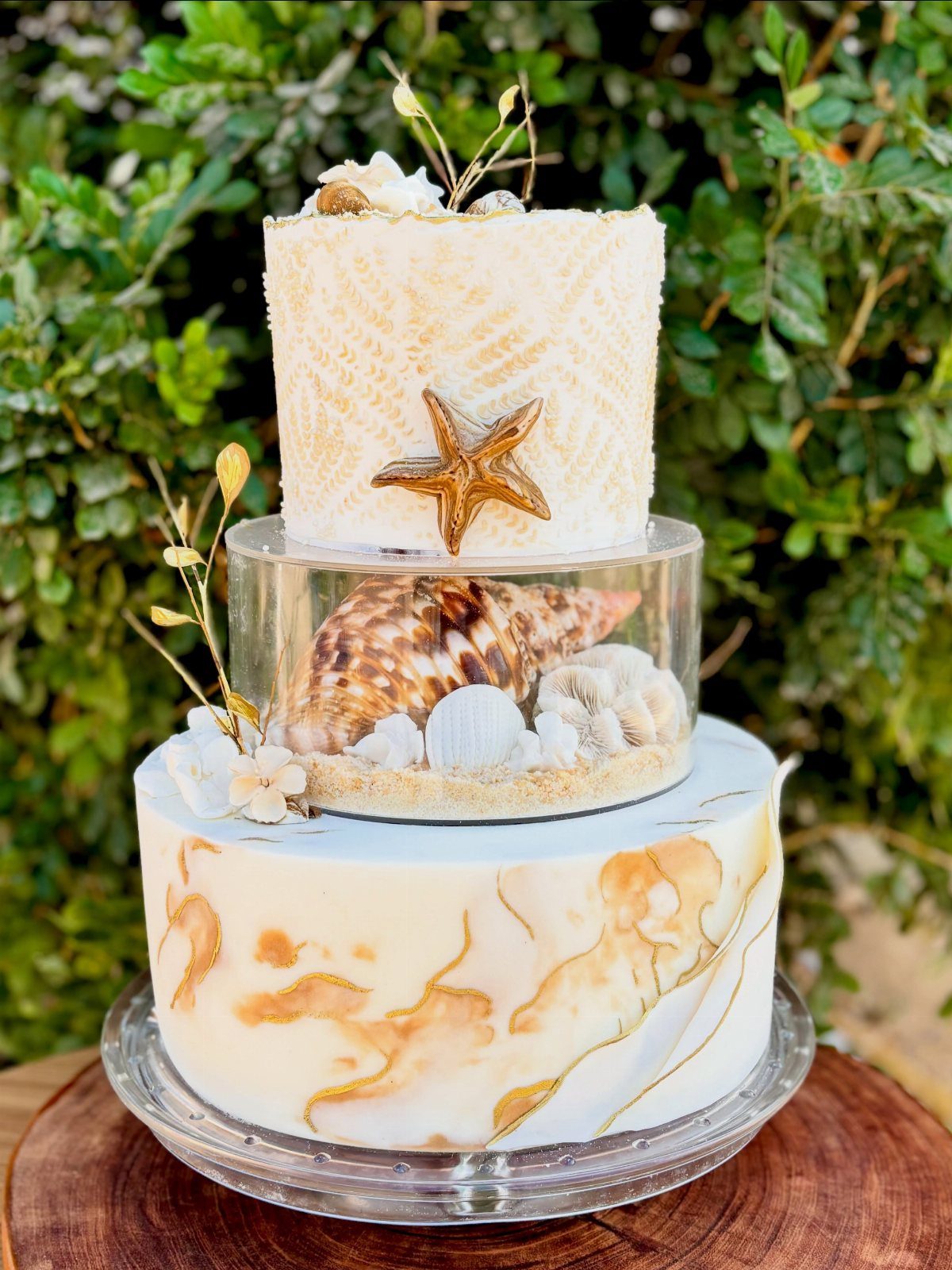 Three-tier beach themed cake with seashells, starfish, and gold marble accents.