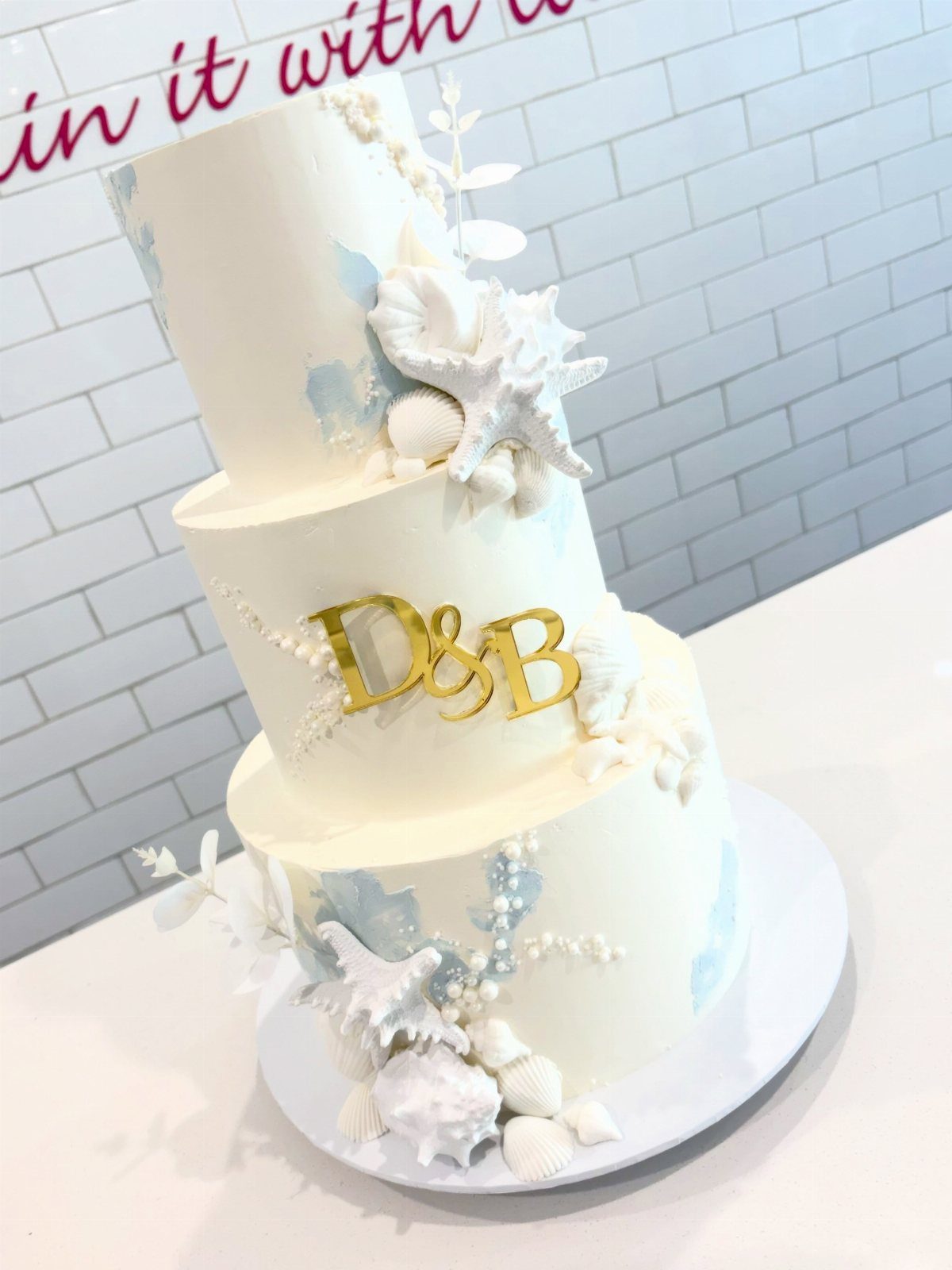 Three-tier white wedding cake with blue accents and edible seashell and starfish decorations.