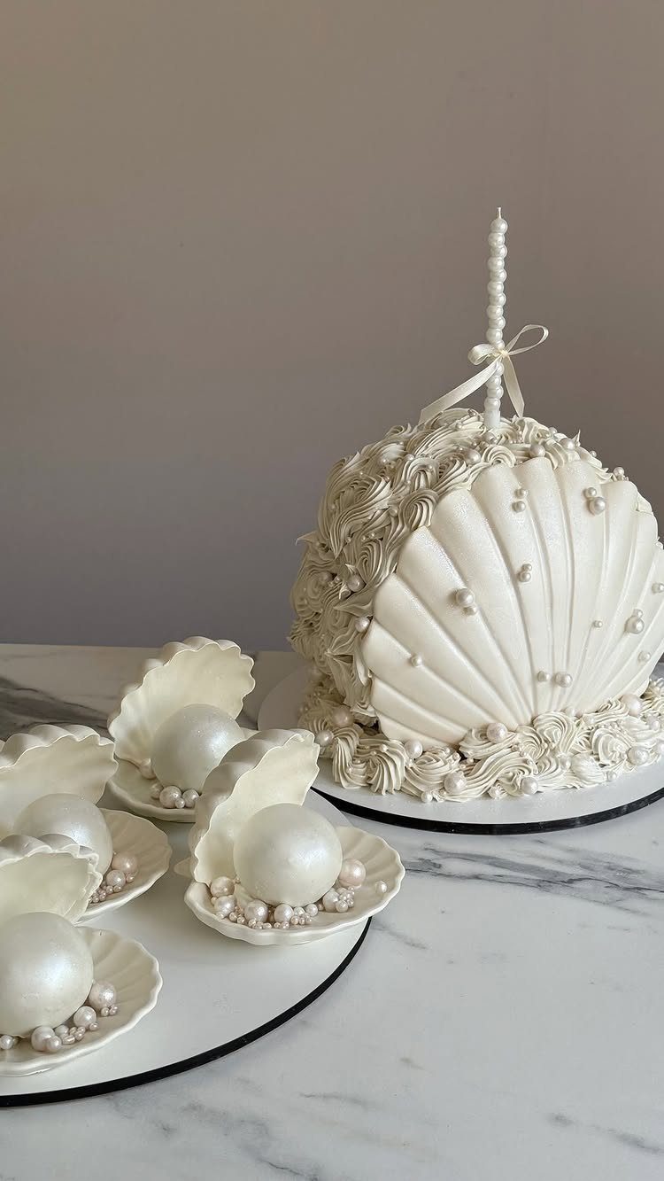 White seashell-shaped wedding cake decorated with pearls and a single white candle.