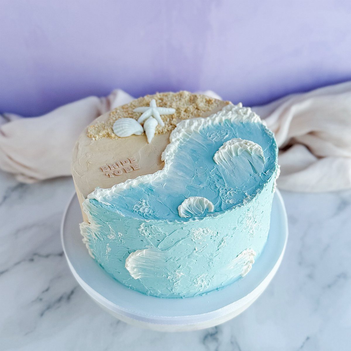 Beach wedding cake with blue textured waves, sandy top, and a white starfish.