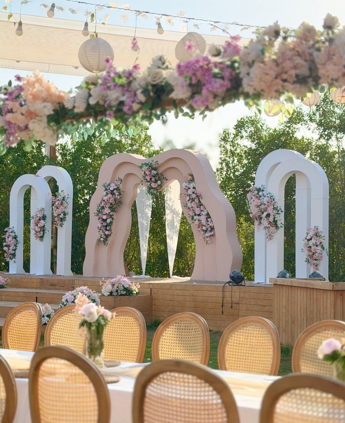 Blush pink and white wedding decor with arched backdrops and woven cane chairs.