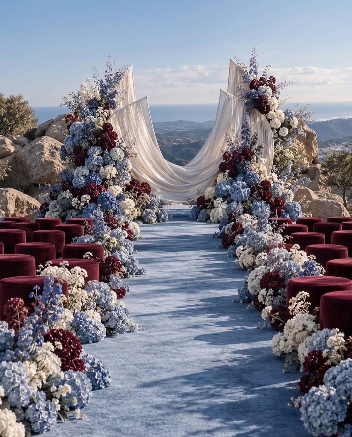 Wedding ceremony setup with burgundy velvet seats and dusty blue floral arrangements outdoors.