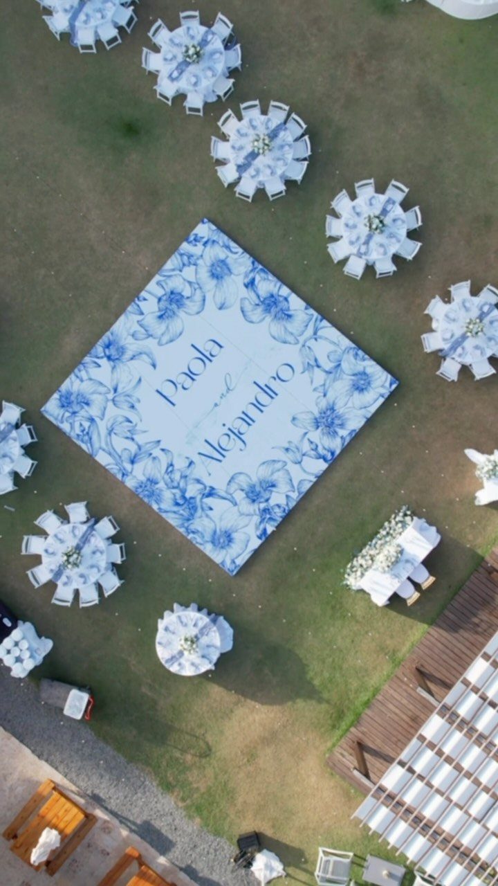 Outdoor wedding reception with white tables and a large blue floral dance floor.