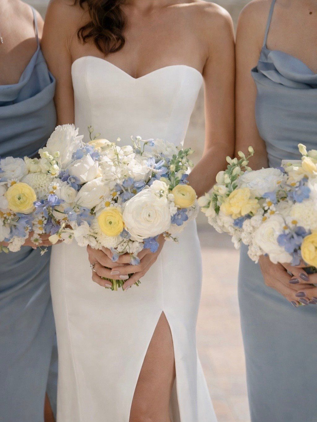 Bride and bridesmaids holding bouquets with yellow and blue flowers in wedding attire