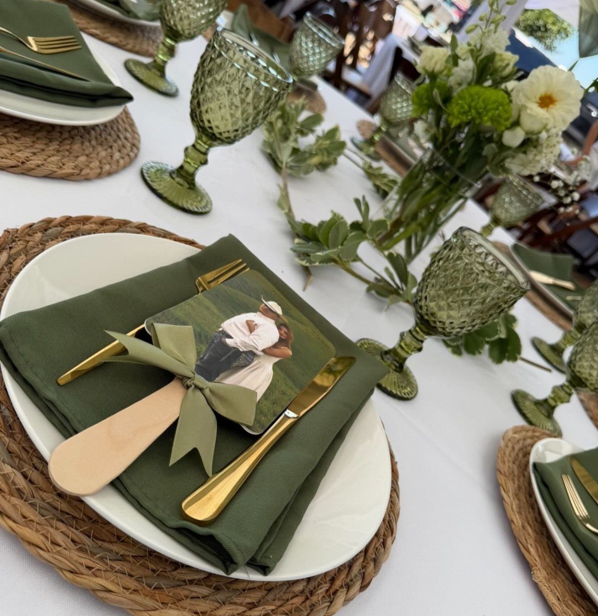 Olive green napkins and gold cutlery on white plates with woven chargers.