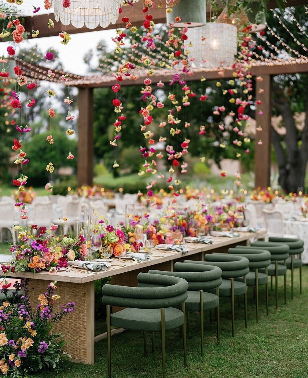 Outdoor wedding table with green chairs and hanging fuchsia and yellow floral arrangements.