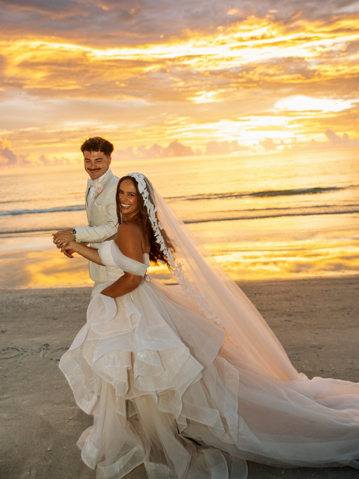 Bride and groom posing on a beach during a golden sunset wedding shoot.