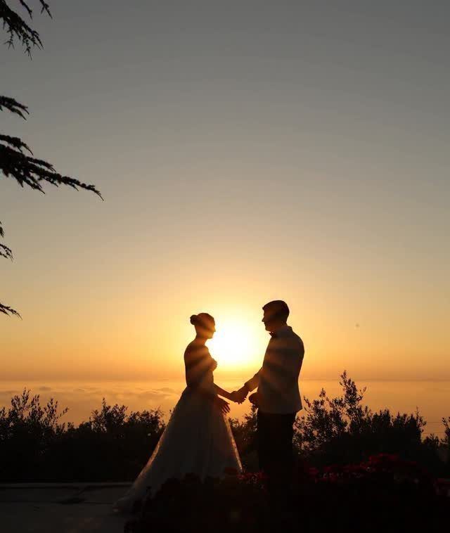Bride and groom silhouettes holding hands against a glowing orange ocean sunset.