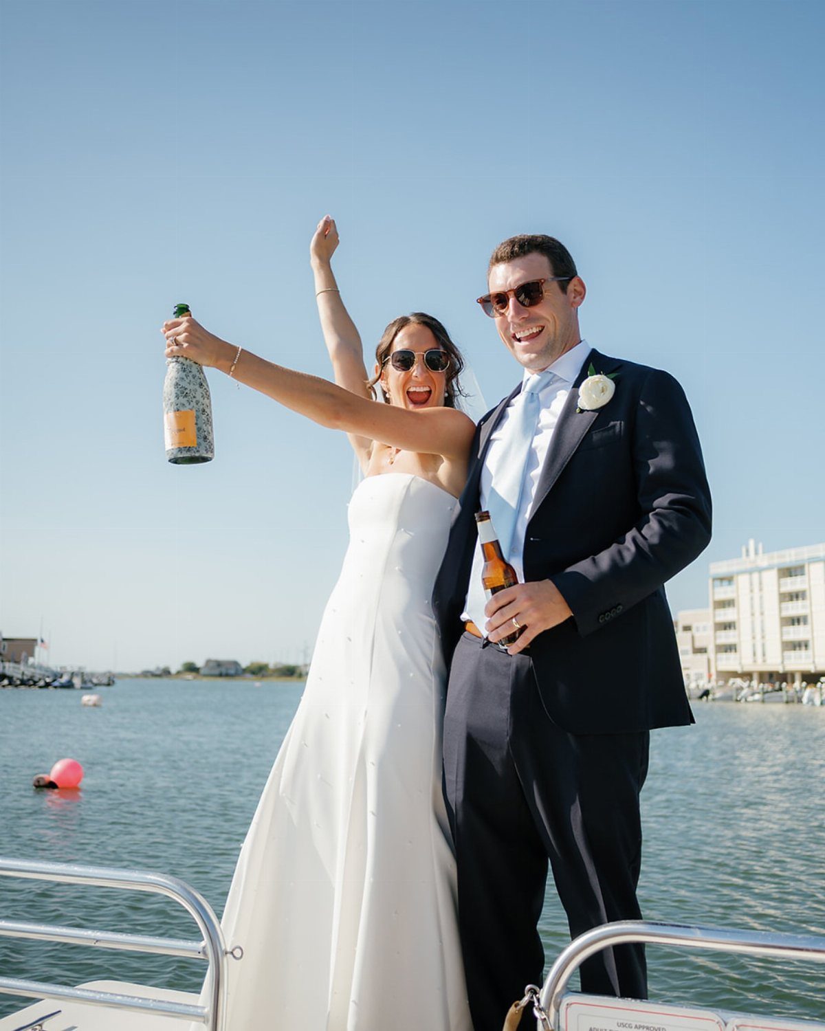 Bride and groom celebrating on a boat with drinks against a coastal backdrop