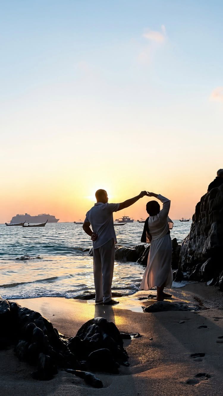 Couple in white wedding clothes dancing on a beach during a golden sunset.