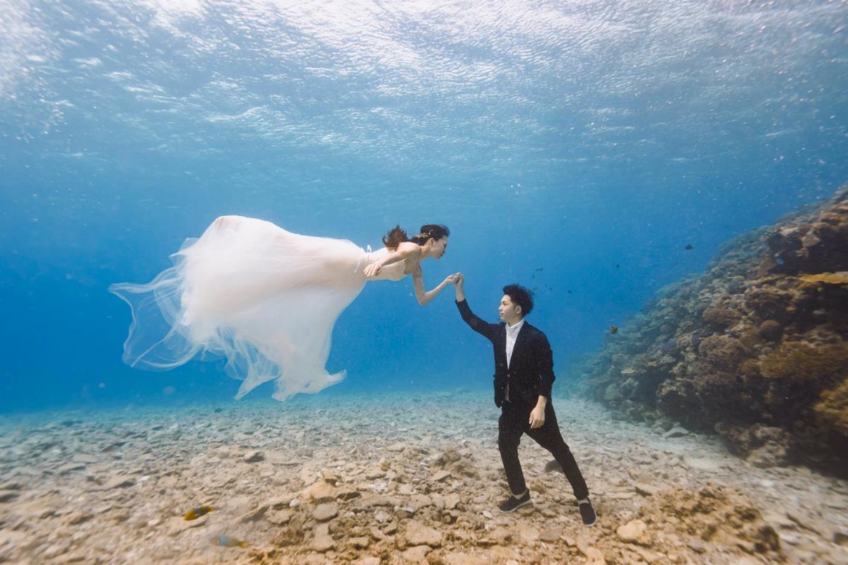 Wedding couple holding hands underwater with a flowing white dress and black suit.