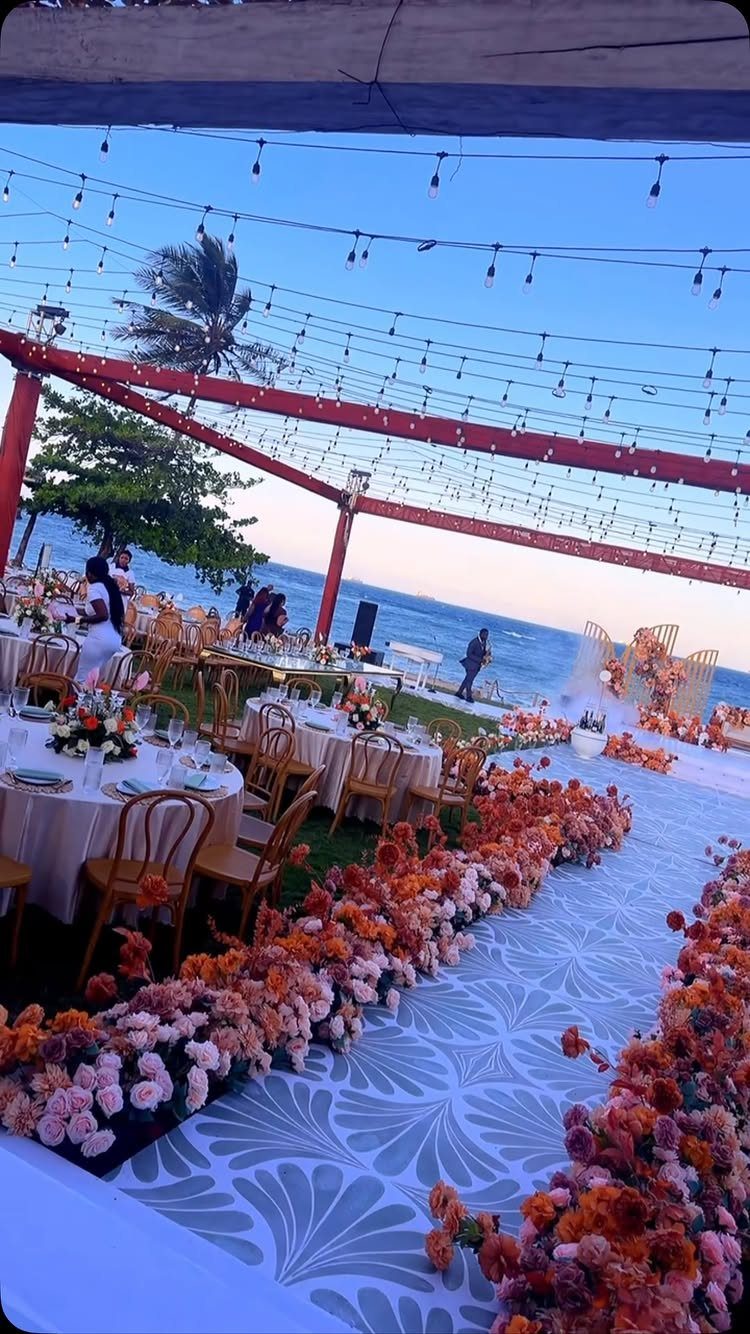Beach wedding reception with floral aisle, round tables, and string lights at dusk.