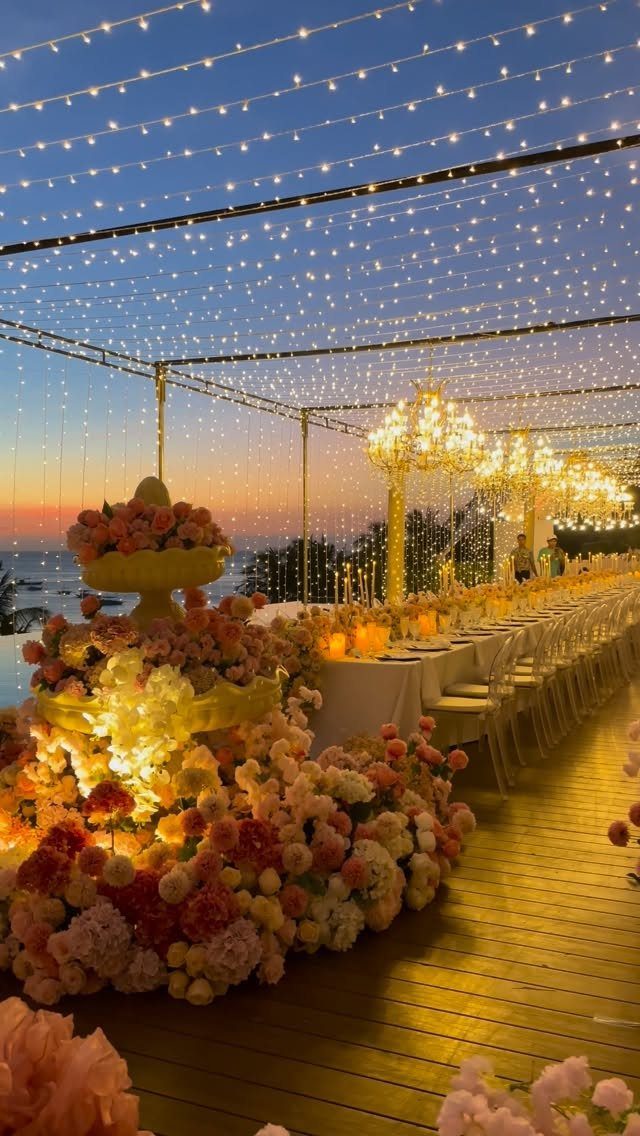 Elegant beach wedding reception with long table, floral arrangements, and fairy light canopy.