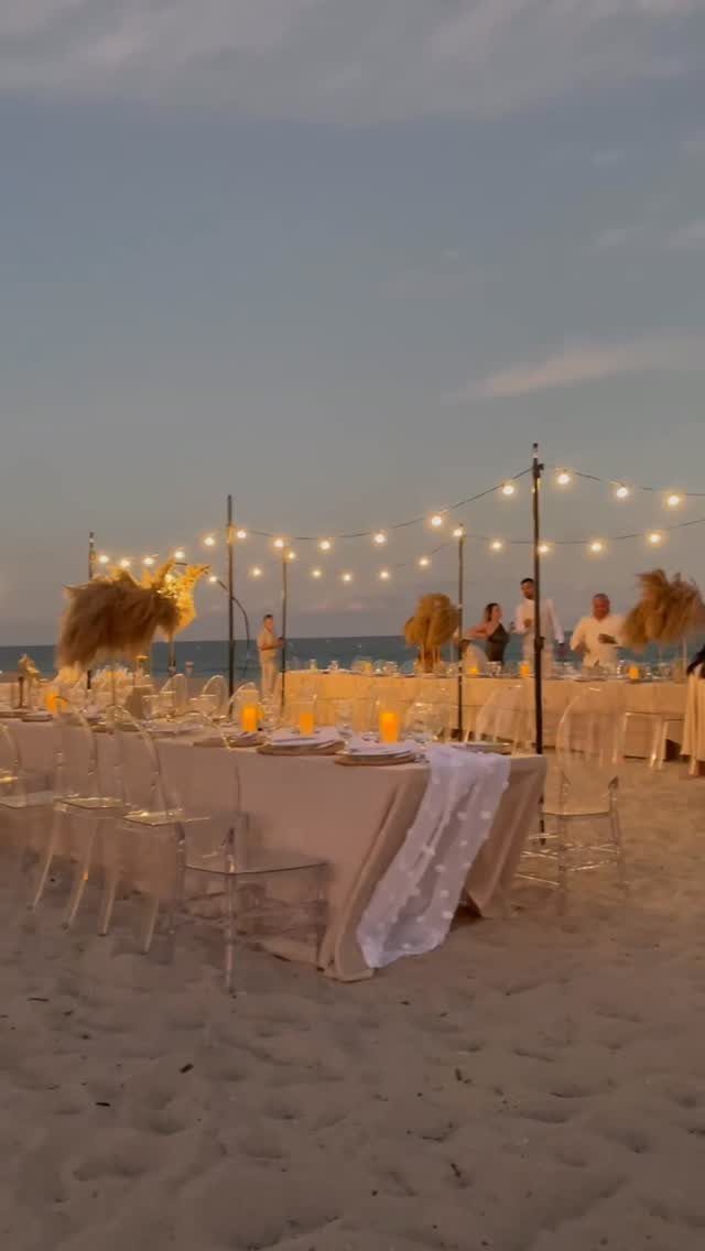 Elegant beach wedding reception table with clear chairs and string lights at dusk