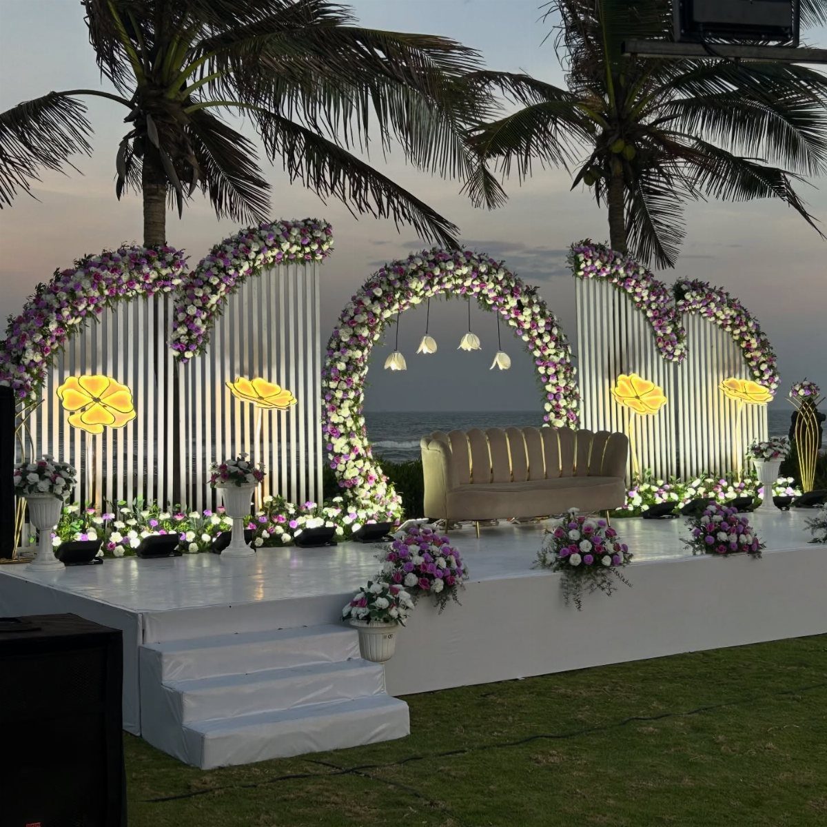 Wedding stage with floral arches and a sofa on a beach at sunset