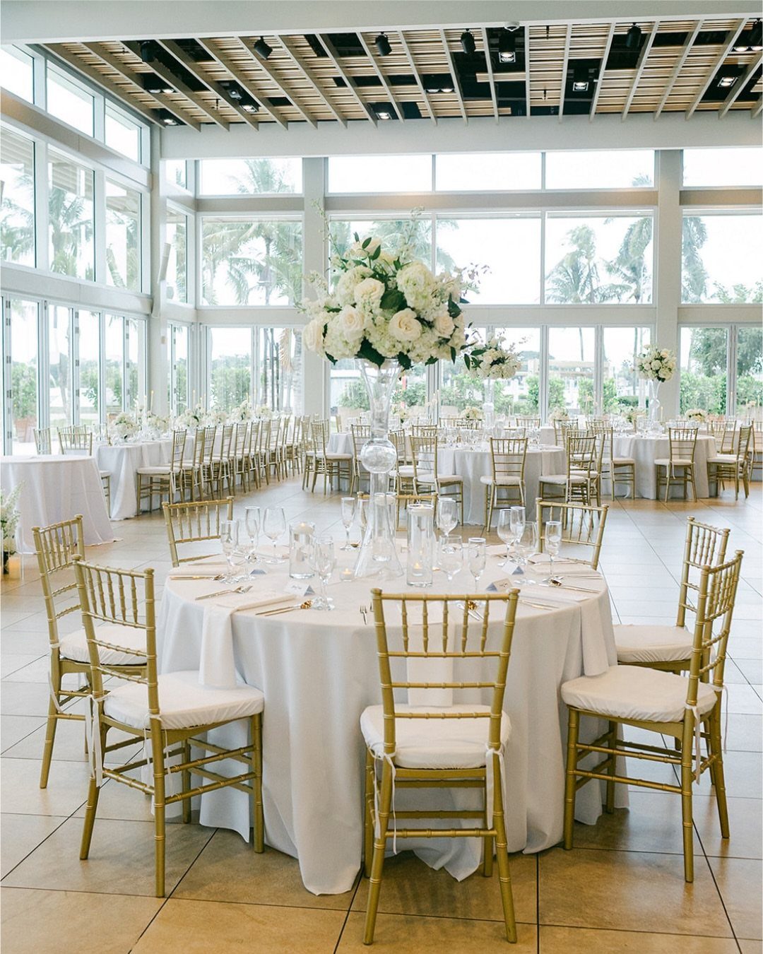 Elegant wedding reception setup with white linens, gold chairs, and coastal views.
