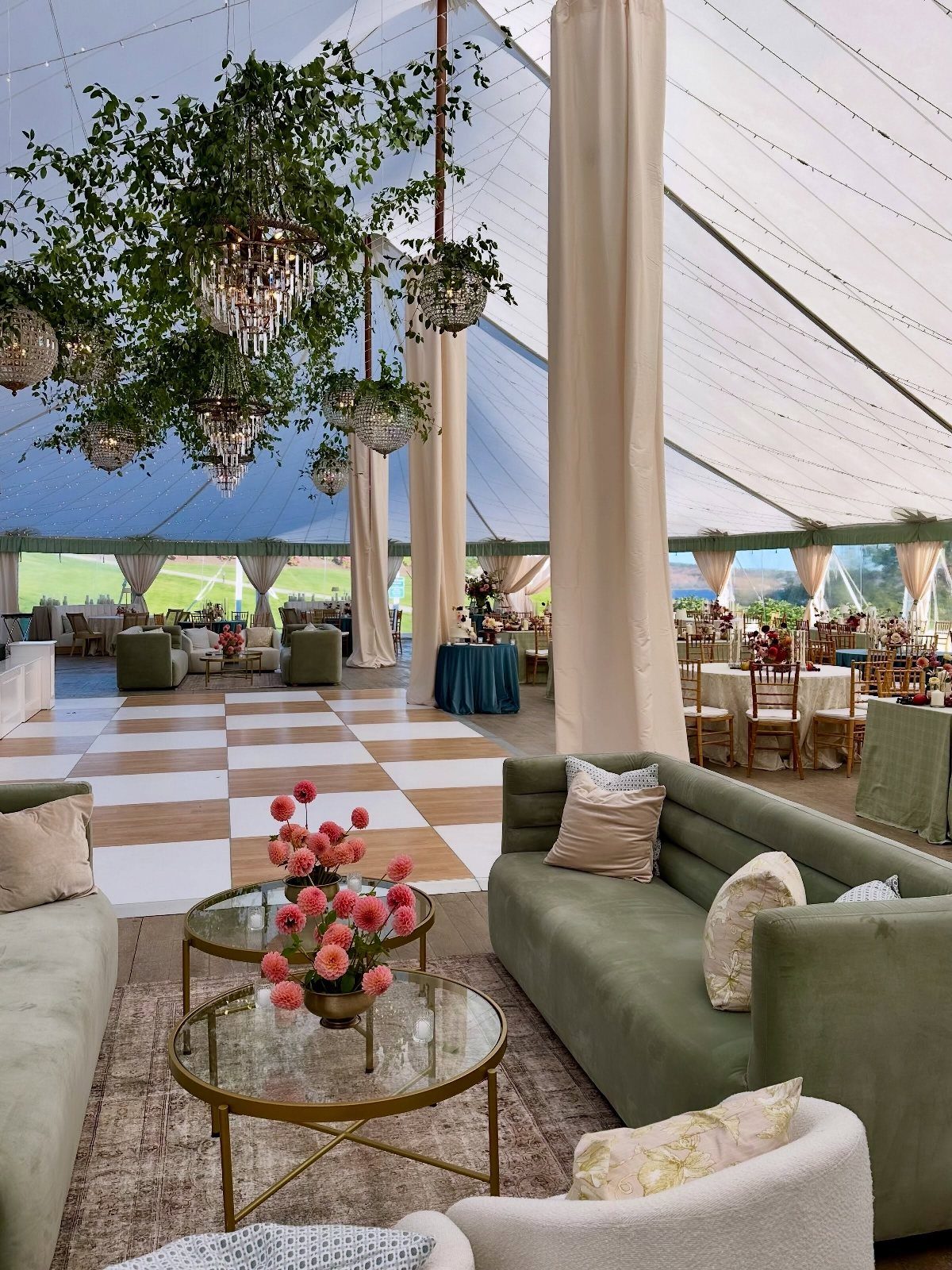 Elegant tent wedding venue with green velvet sofas, chandeliers, and hanging greenery.