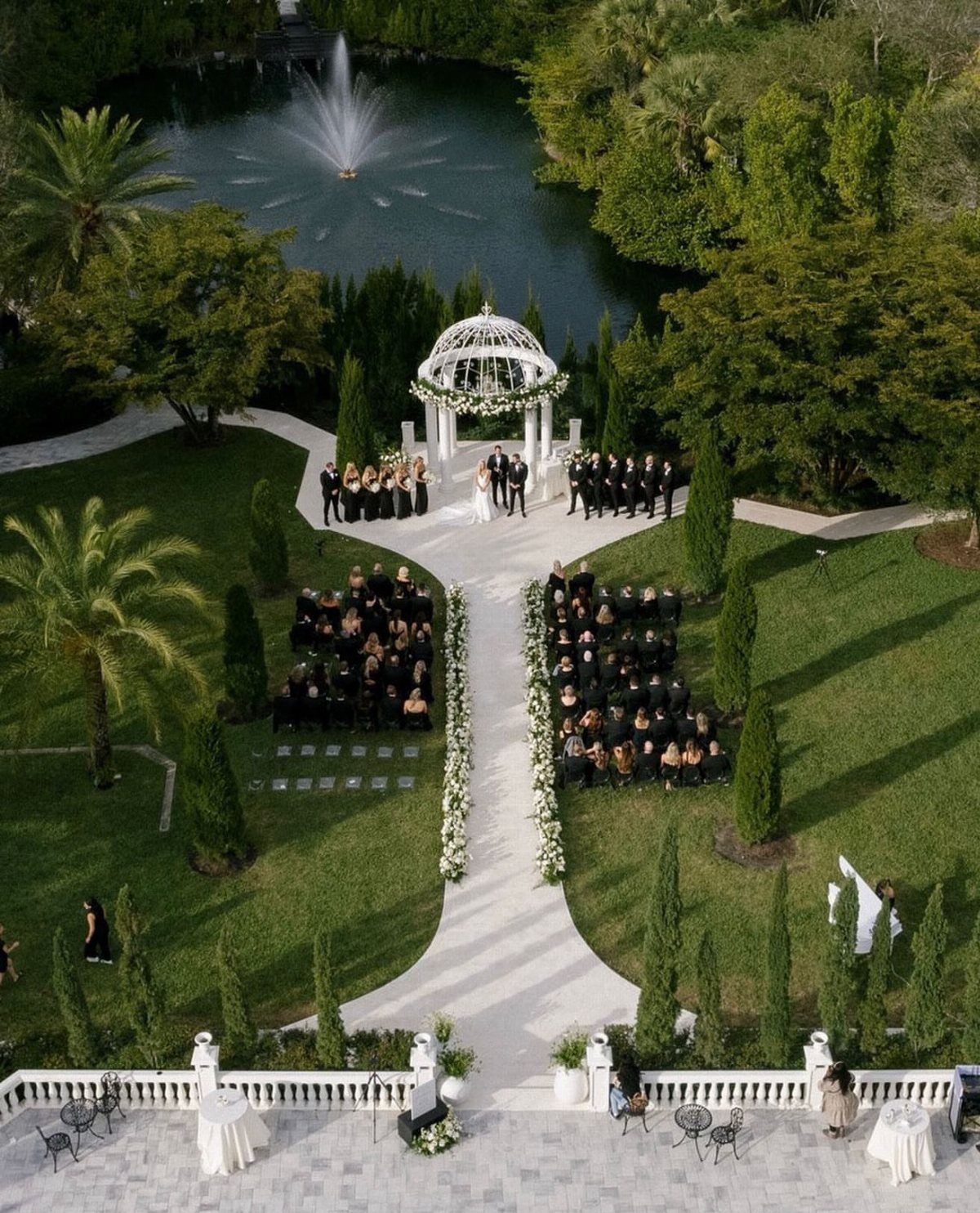 Outdoor wedding ceremony in a garden with a white gazebo and pond fountain.