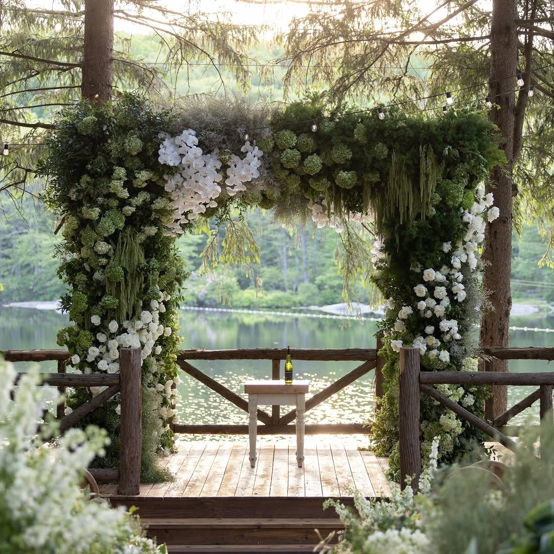Floral wedding arch on a wooden deck overlooking a serene lake and forest