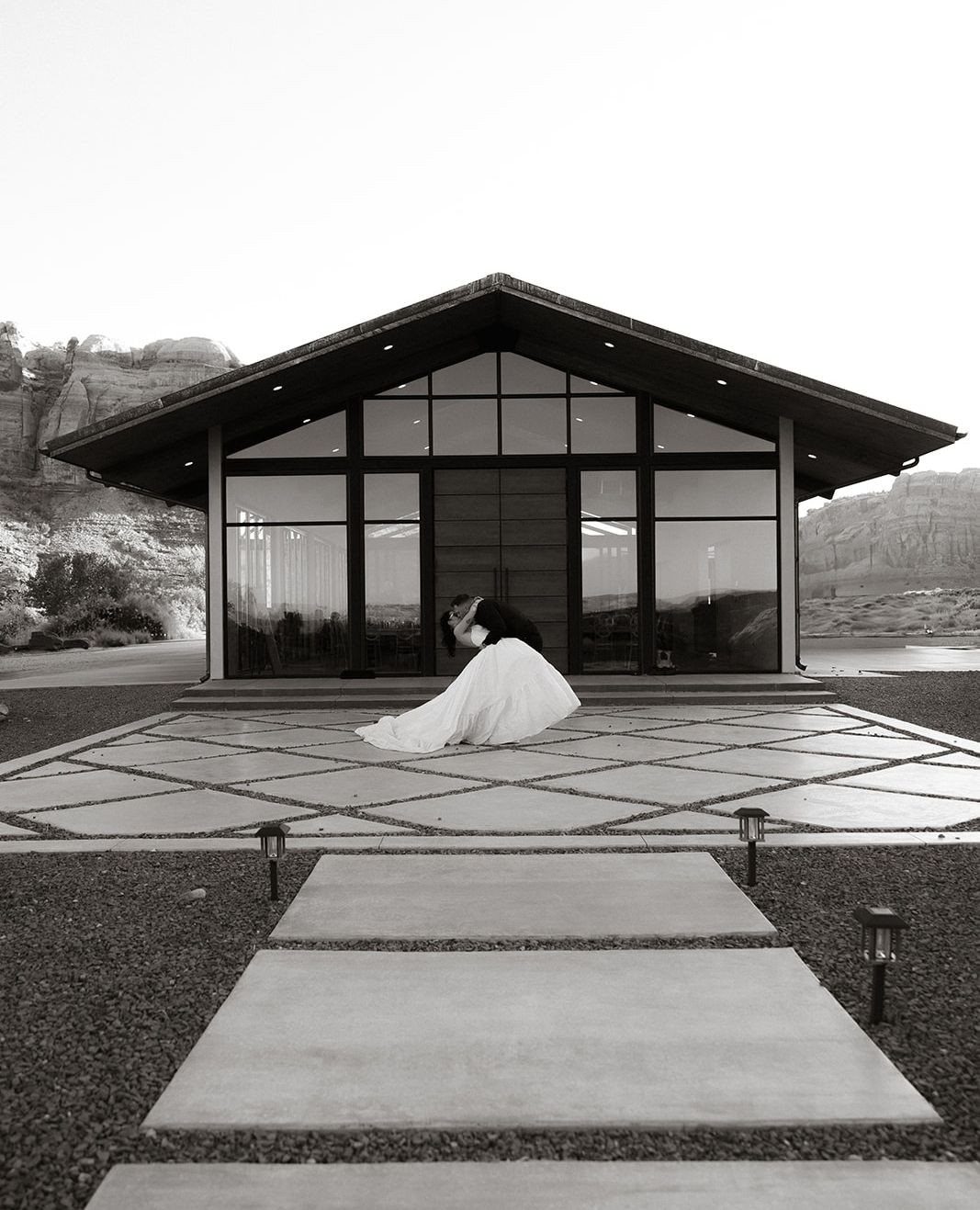 Bride in white dress sitting before a modern glass venue in Moab desert