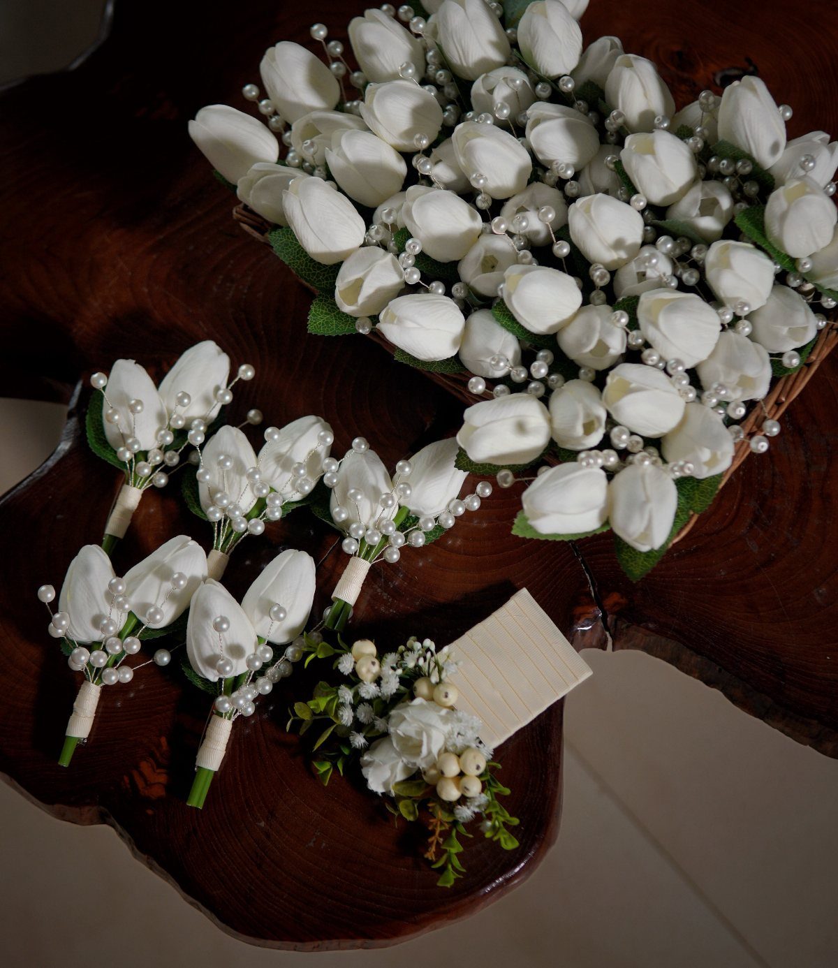 White artificial tulip bouquets with pearls resting on a dark rustic wooden table