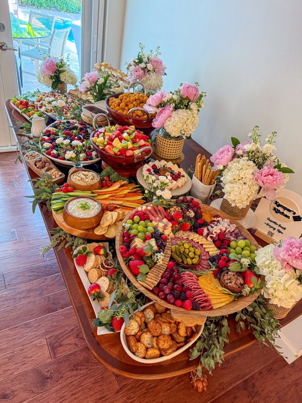 Lavish food spread with fruit and charcuterie on a wooden table with flowers