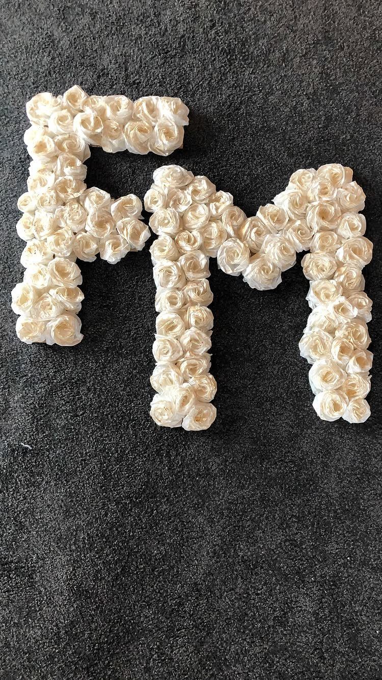 Letters F and M made of cream artificial roses on a dark grey background