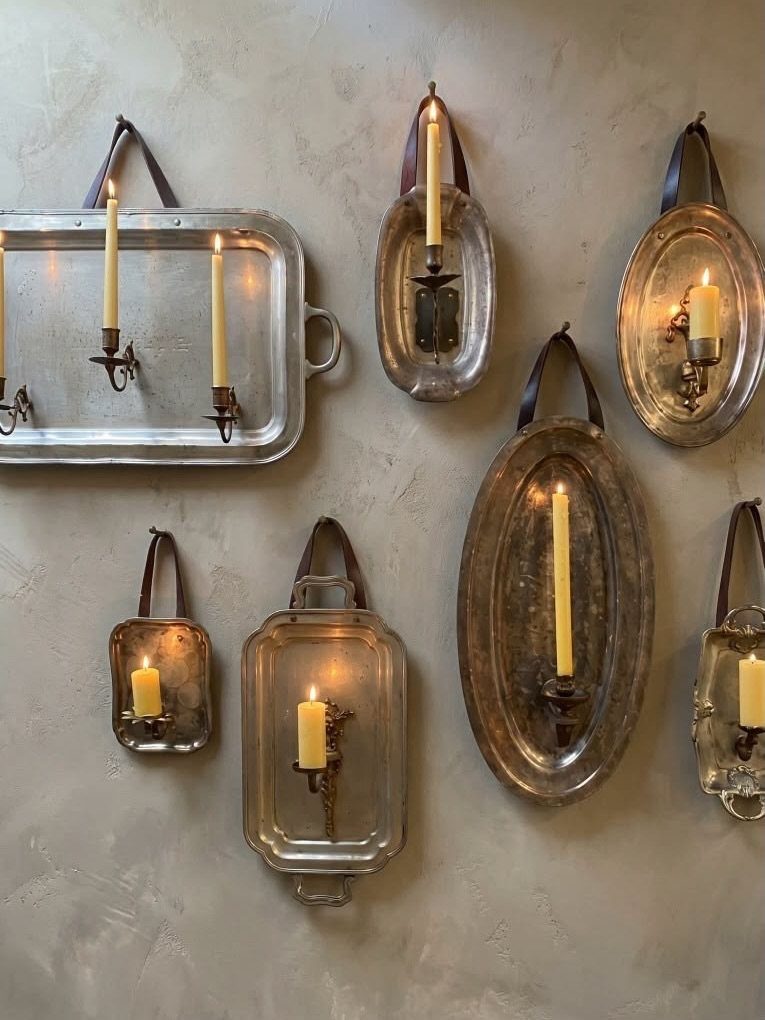 Silver metal trays mounted on a wall holding lit yellow taper candles