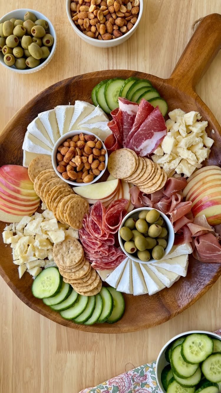 Charcuterie board with cheeses, meats, crackers, fruits, and vegetables on a wooden platter.
