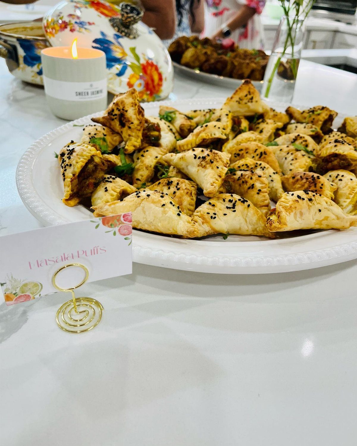 Masala puffs with sesame seeds on a white platter with a name card.