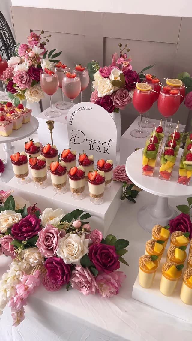 Dessert bar with strawberry cheesecake cups, fruit skewers, and pink floral arrangements.