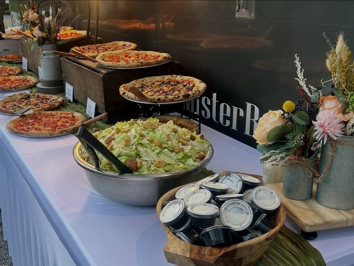 Buffet table with various thin-crust pizzas and a large bowl of Caesar salad.