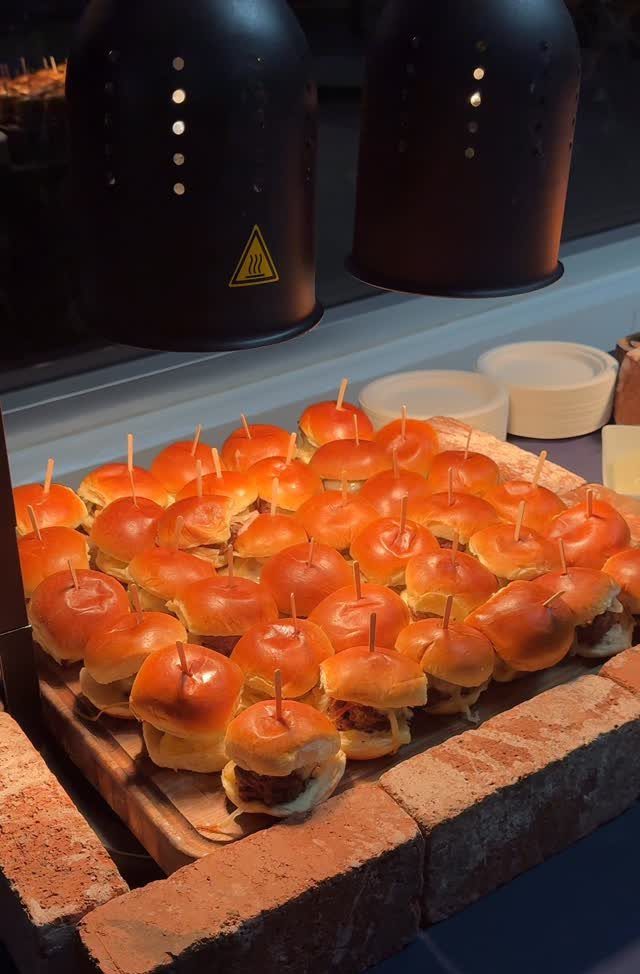 Mini sliders on a wooden platter resting on a red brick ledge.