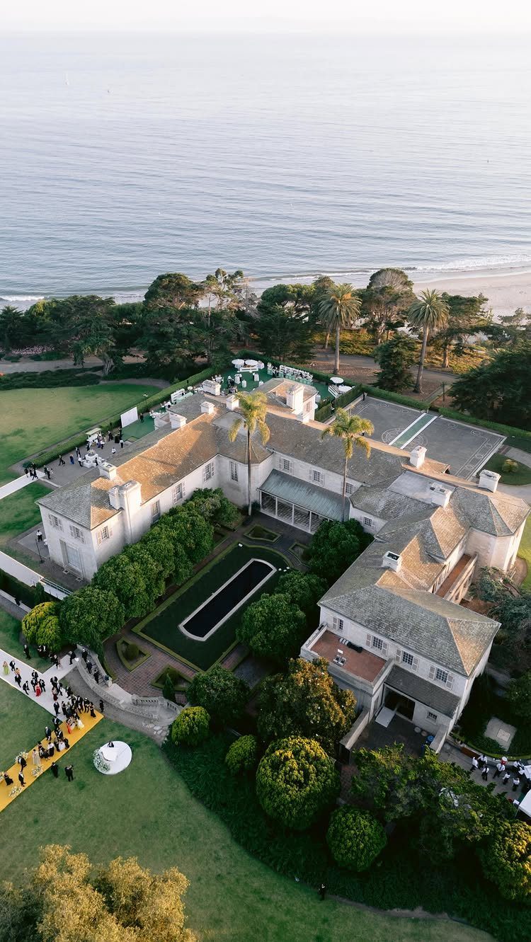 Large white luxury estate with a pool overlooking the ocean coastline and beach.