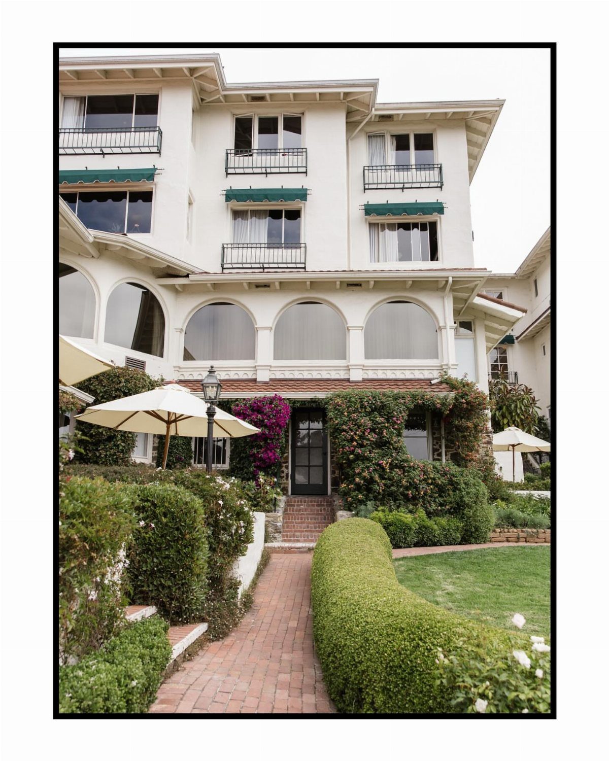 White Mediterranean-style estate with arched windows and manicured gardens and brick walkway.
