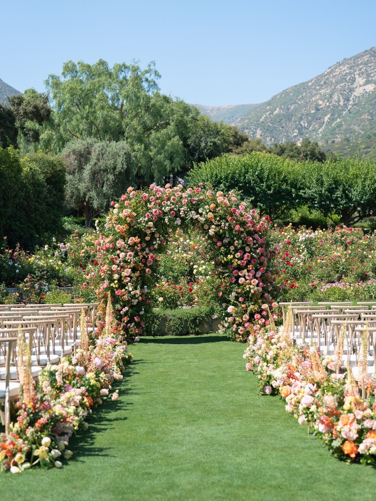 Floral wedding arch and aisle with wooden chairs in a lush mountain garden