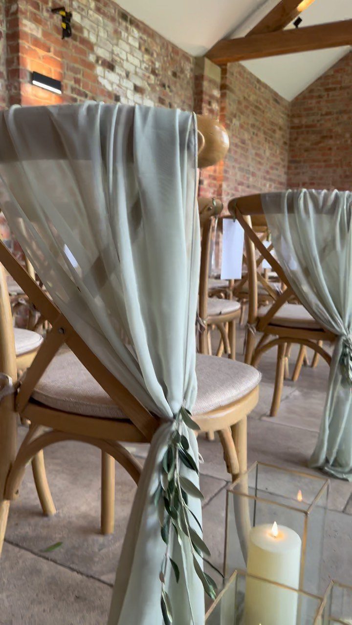 Wooden chairs draped in pale green fabric and greenery with a lit candle.