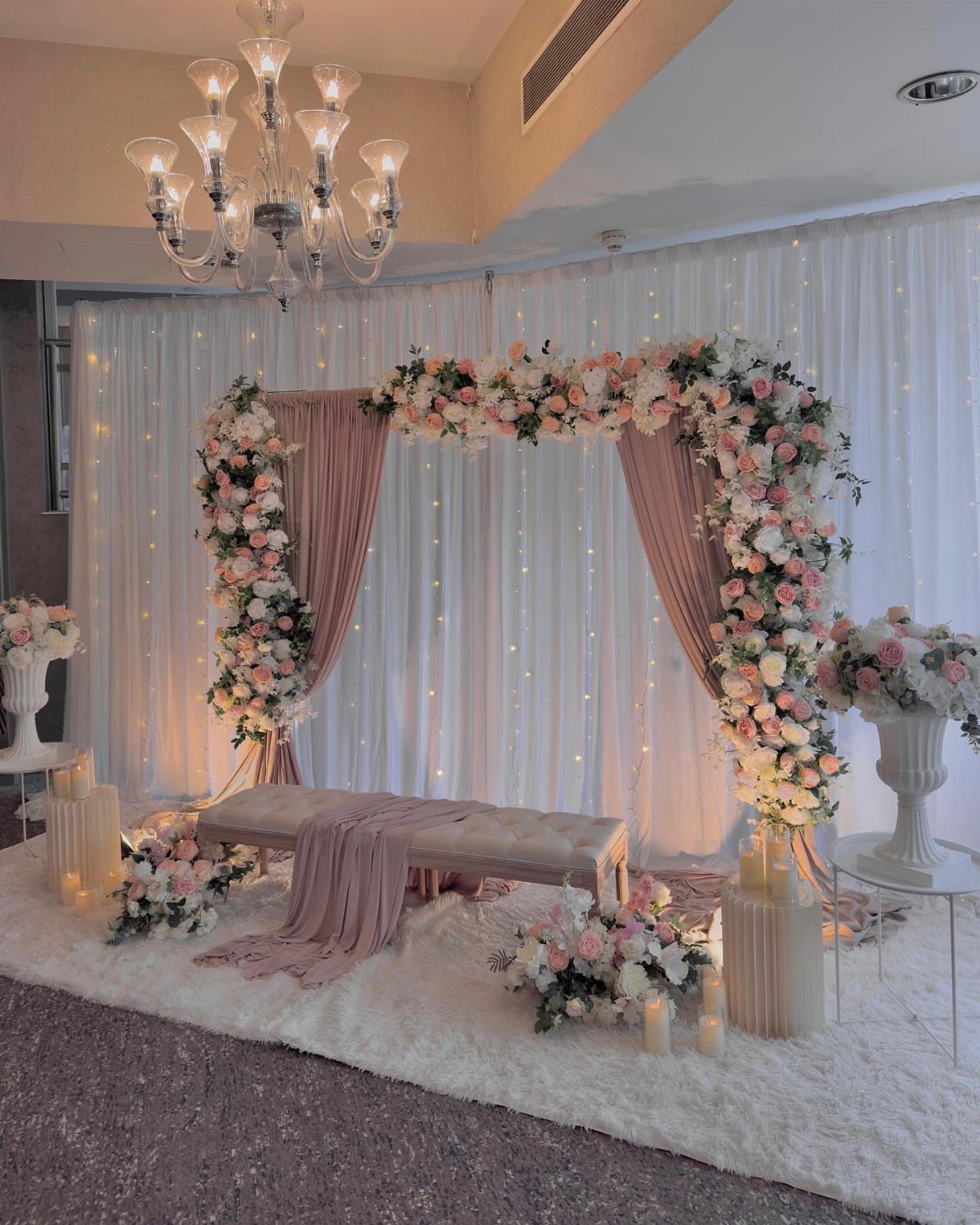 Floral arch with pink drapes and fairy lights backdrop for a wedding ceremony.